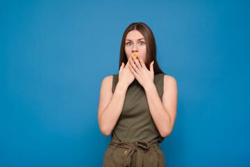 Young beautiful caucasian woman in a green t-shirt on an isolated blue background surprised. Covers his face with his hands