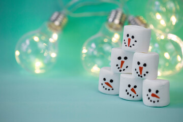 marshmallow snowman on mint turquoise background with garland lighting