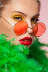 Blonde young women wearing round frame sunglasess and green feather boa