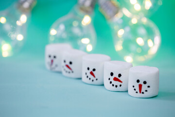 marshmallow snowman on mint turquoise background with garland lighting