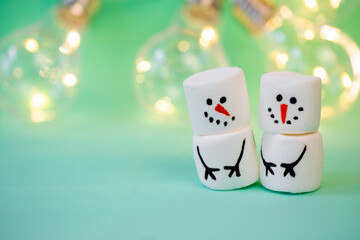 marshmallow snowman on mint turquoise background with garland lighting
