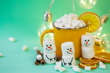 Fototapeta na wymiar marshmallow snowmen on a mint turquoise background with a yellow cocoa mug illuminated by a garland
