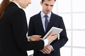 Fototapeta premium Businessman and woman using tablet computer for discussing questions in office. Partners or colleagues at meeting. Business cooperation concept