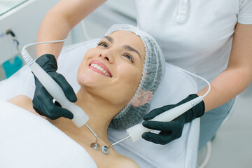 Excited woman undergoing micro current therapy in beauty salon