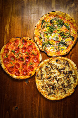 Three pizzas on a wooden surface