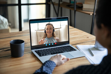 Shoulder back view young indian woman holding video call online meeting with smiling european...