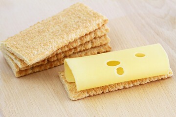 Slice of swiss cheese on crisp bread on wooden board
