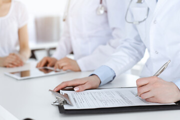 Unknown woman-doctors at work consulting patient. Female physicians filling up medical documents or prescription, close-up