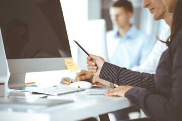 Business woman and man are discussing questions while using computer and blocknote in modern office, close-up. Teamwork in business