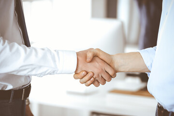 Fototapeta na wymiar Two businessmen are shaking hands in office, close-up. Happy and excited business woman stands with raising hands at the background. Business people concept