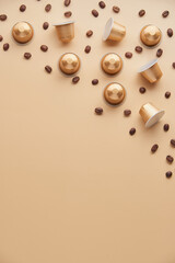 Caffeine, hot drinks and objects concept - close up of golden capsules or pods for coffee mashine with some roasted grains on beige background. Top view with space for text. Flat lay..