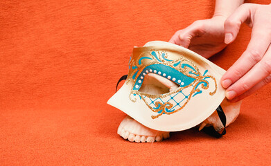 Hand placing human skull with a carneval mask on orange background, profile perspective, human anatomy