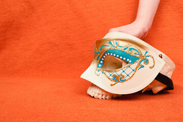 Hand placing human skull with a carneval mask on orange background, profile perspective, human anatomy