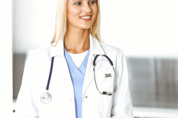 Fototapeta premium Woman-doctor at work in hospital is happy to communicate with female patient. Blonde physician checks medical history record and exam results. Medicine concept