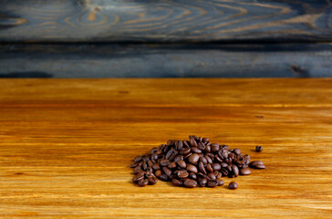 Heap of roasted coffee beans on a table made of wooden brown boards. Copy space for text.