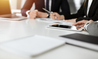 Unknown businessmen and woman sitting, using laptop computer and discussing questions at meeting in sunny office, close-up. Success concept