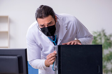 Young male doctor with stethoscope repairing computer