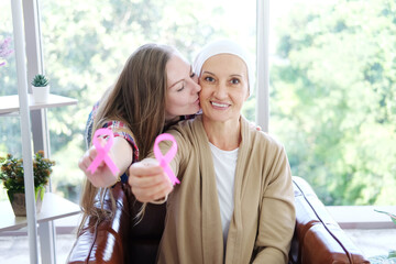 Caucasian daughter kiss Elderly mother in white headscarf is smiling and holding Awareness pink ribbon of common cancer is symbol of various campaign activities for patients with breast cancer.