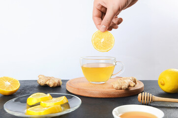 Hand putting lemon in ginger tea cup on wooden desk