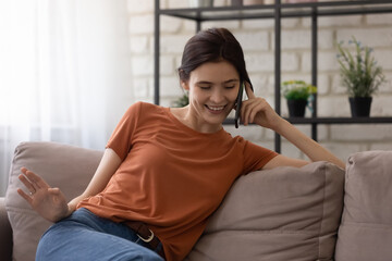 Relaxed millennial pretty woman sitting on sofa, holding mobile phone call conversation with friends or family, sharing life news, telling rumors chatting communication distantly, modern tech concept.