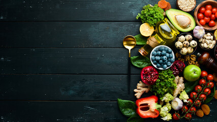 Food background: A set of healthy and clean food - vegetables, fruits, fish, meat, nuts and greens. On a black stone background. Top view. Free copy space.