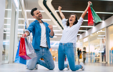 Fototapeta premium Excited winning couple in love or family with paper bags in hands while are shouting during shopping in the mall