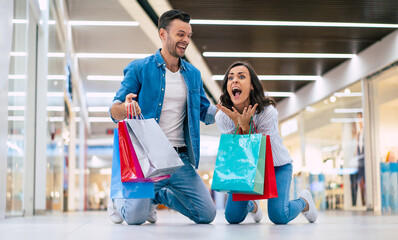  Excited winning couple in love or family with paper bags in hands while are shouting during shopping in the mall