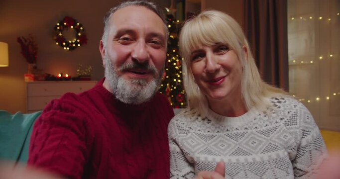 POV of happy smiling Caucasian senior married couple in festive mood video chatting on intrnet at home in decorated room on New Year. Merry Christmas concept. Video call online. Close up portrait