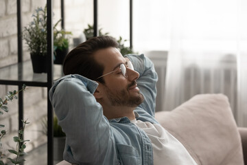 Side head shot view calm serene young 30s man in eyeglasses resting on cozy sofa with closed eyes...
