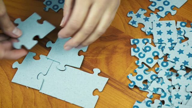 Close-up of a young girl hand collecting jigsaw puzzles on a surface.