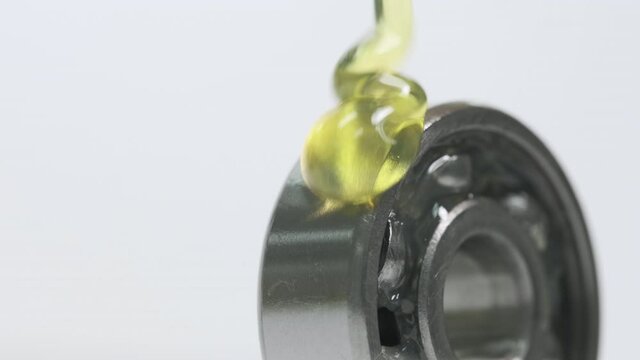 Closed up macro, Pouring yellow oil into ball bearing isolated on white backgroud with copy space. Oil help to protect wear and rust. Reduce friction. Engineering, service and industrial concept