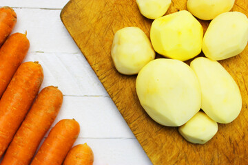 peeled round potatoes a huge pile of very large fresh and sweet carrots on a white wooden table. beautiful fresh market organic carrots in a large pile close-up full frame healthy food and healthy