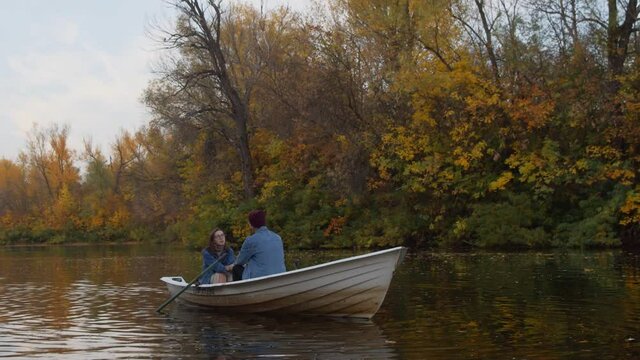 A handsome guy and a beautiful girl sits in a boat on a lake in a fairy autumn forest
