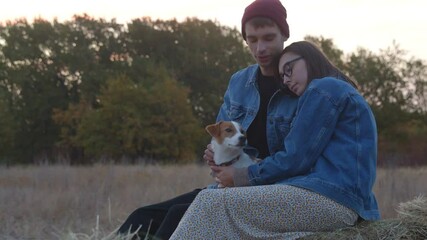 Romantic young couple with jack russell terrier dog sits on haystack in evening