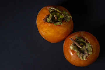 Persimmon on a black background. Two persimmons lie next to each other. Healthy fruits