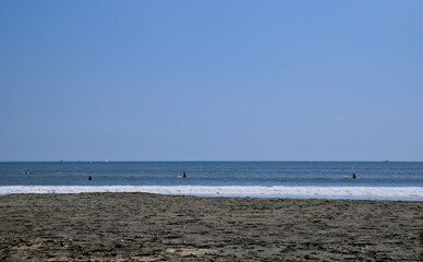 Daytime view of the ocean from Katase Higashihama Beach on a clear day, with several surfers and boats visible in the distance