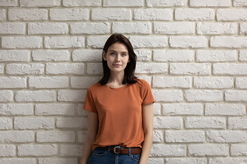 Portrait of pretty young 20s smiling european appearance woman isolated on brick wall background, confident millennial happy caucasian youth generation representative in casual wear looking at camera.