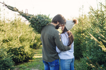 Back view of young lovely couple with christmas tree at garden centre before holidays. Happy winter holidays concept.