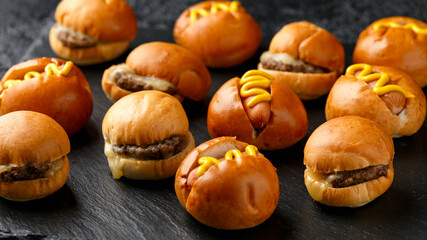 Mini hamburgers, burger and hot dogs with yellow mustard on black slate board