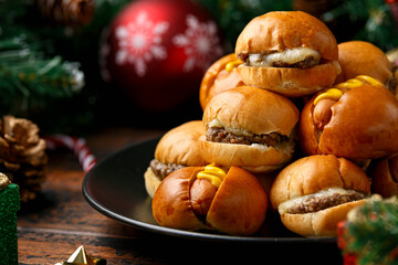 Christmas mini hamburgers, burger and hot dogs with decoration, gifts, green tree branch on wooden...