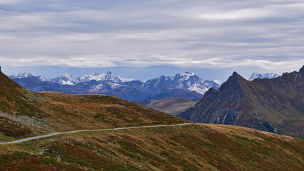 Beautiful panorama view of the snow-covered alpine mountains of Rätikon near Gargellen, Montafon valley, Alps, Austria with a hiking trail leading through meadows in autumn season with cloudy sky.