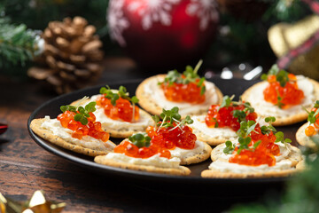 Salmon caviar and soft cheese savory crackers with decoration, gifts, green tree branch on wooden rustic table.