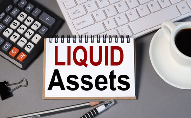 liquid assets. text on white paper on gray background near calculator and keyboard with a cup of...