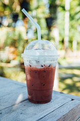 Iced cocoa or coffee drink with milk froth on wooden table in the garden