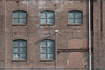 Fototapeta premium A fragment of an old and weathered facade of an old factory, made of masonry, steel and wooden frames.