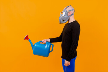 Funny strange man in respirator posing with blue watering pot over orange background