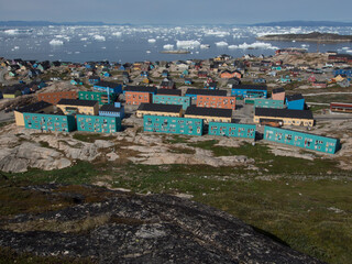 View across a Greenland bay from a rocky outcrop shows drifting ice bergs and traditional coloured housing in the foreground © Tony Skerl