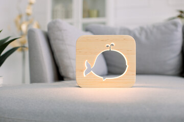 Wooden hand made accessories. Wooden night lamp with whale picture, on gray monochrome sofa, at stylish light home living room interior. Home decor and lamps.