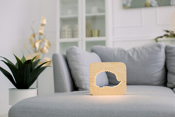 Wooden night lamp with hedgehog cut out picture, on gray sofa, at stylish light home living room interior. Home decor and lamps. Wooden hand made accessories