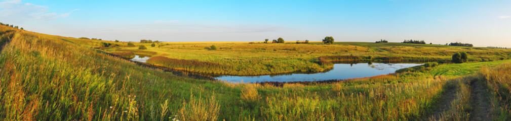 Summer panoramic landscape with river and green hills at sunset